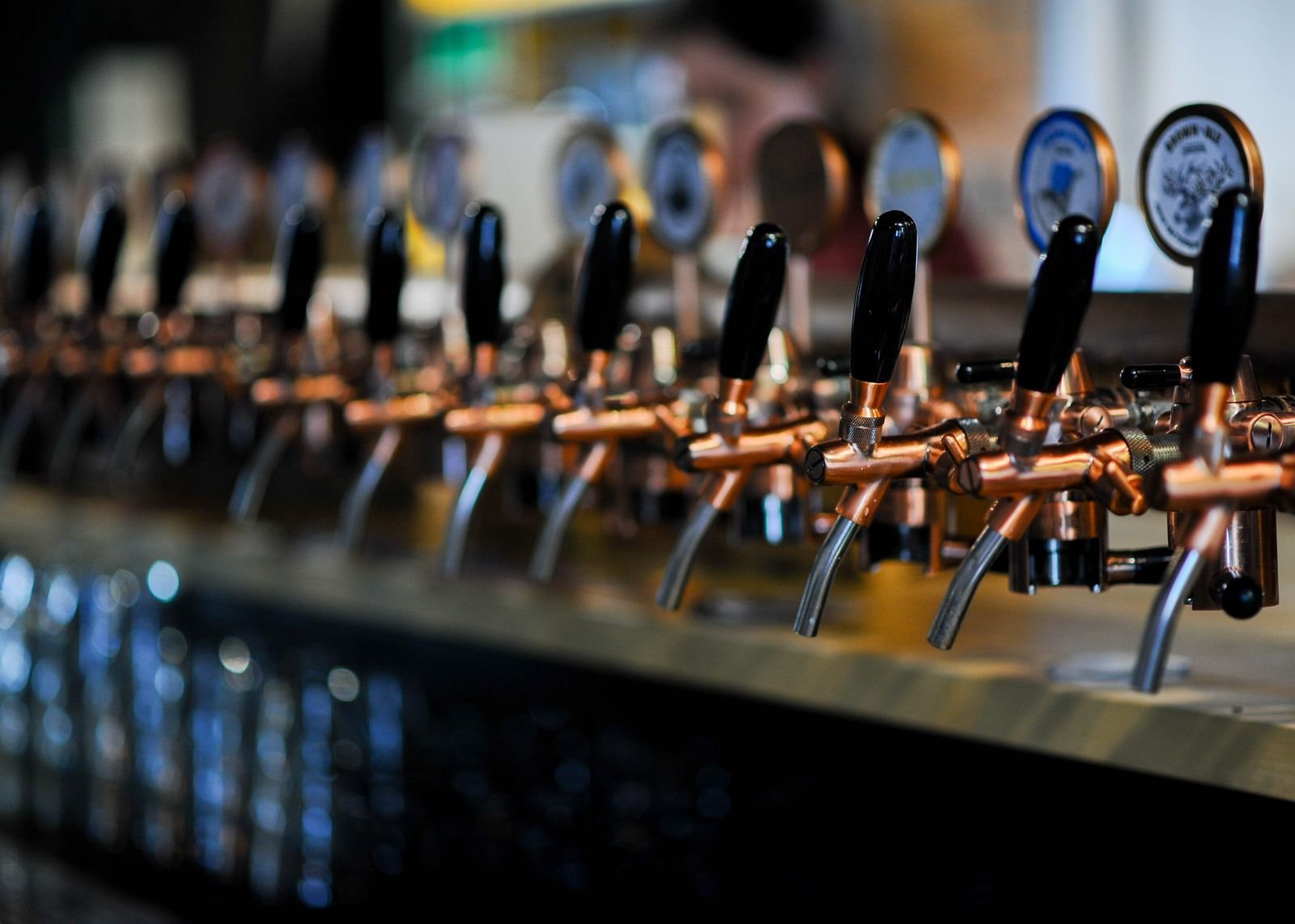 Row of copper draft taps with black handles along the taproom bar in warm low light